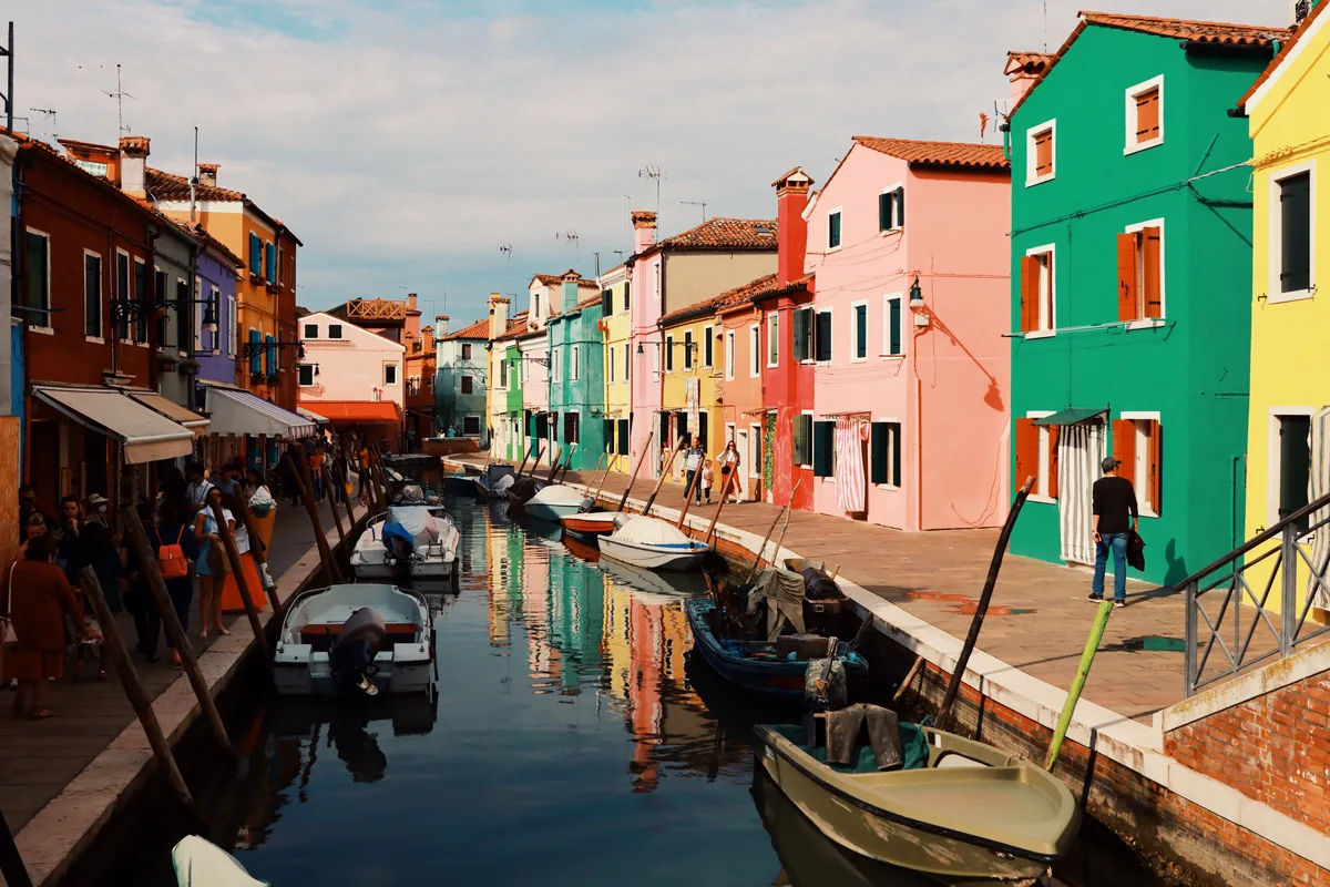 Brightly painted houses in red, green, pink and yellow lining a canal on Burano, one of the islands the cruise route passes
