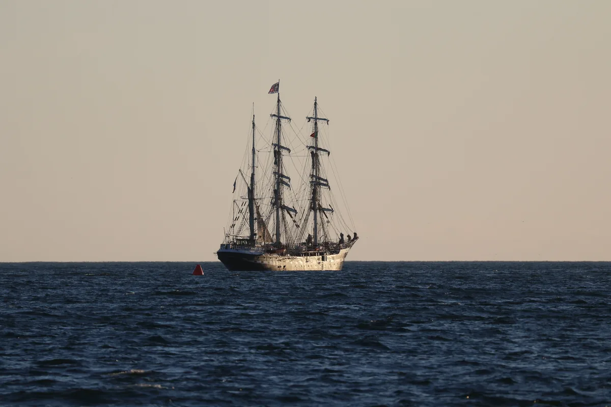 A tall wooden sailing ship on open water at dusk, representative of a galleon-style vessel
